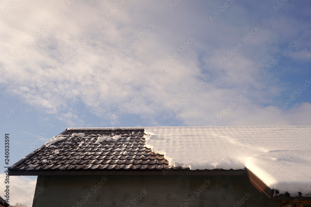 Snow on the roof of the house against the blue sky 