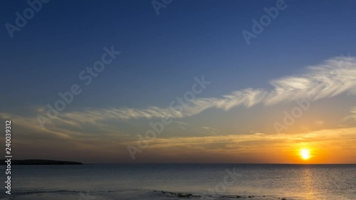 4k timelapse clouds crossing the amazing sky over the sea or ocean at sunset. Sun rays emerge through the clouds. The clouds cross slowly from right to left and appear to be orange blue and purple. 