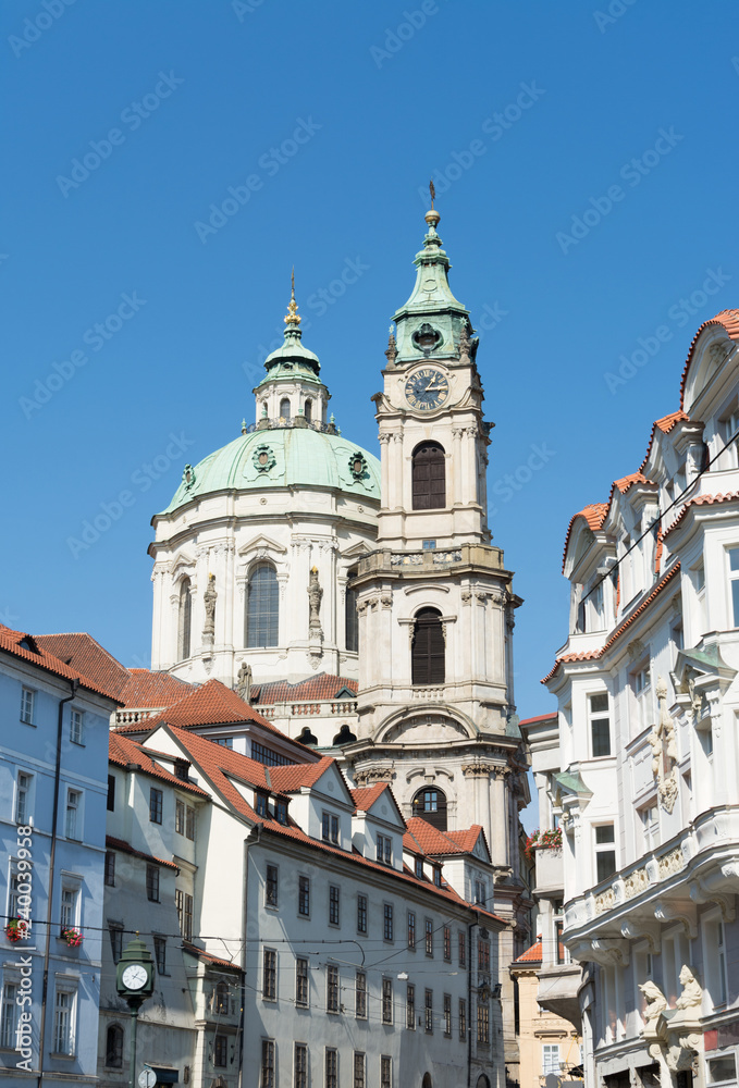 Urban street with the view of St. Nicholas Church on a beautiful summer day, with the clear blue sky, in Prague, Czech Republic
