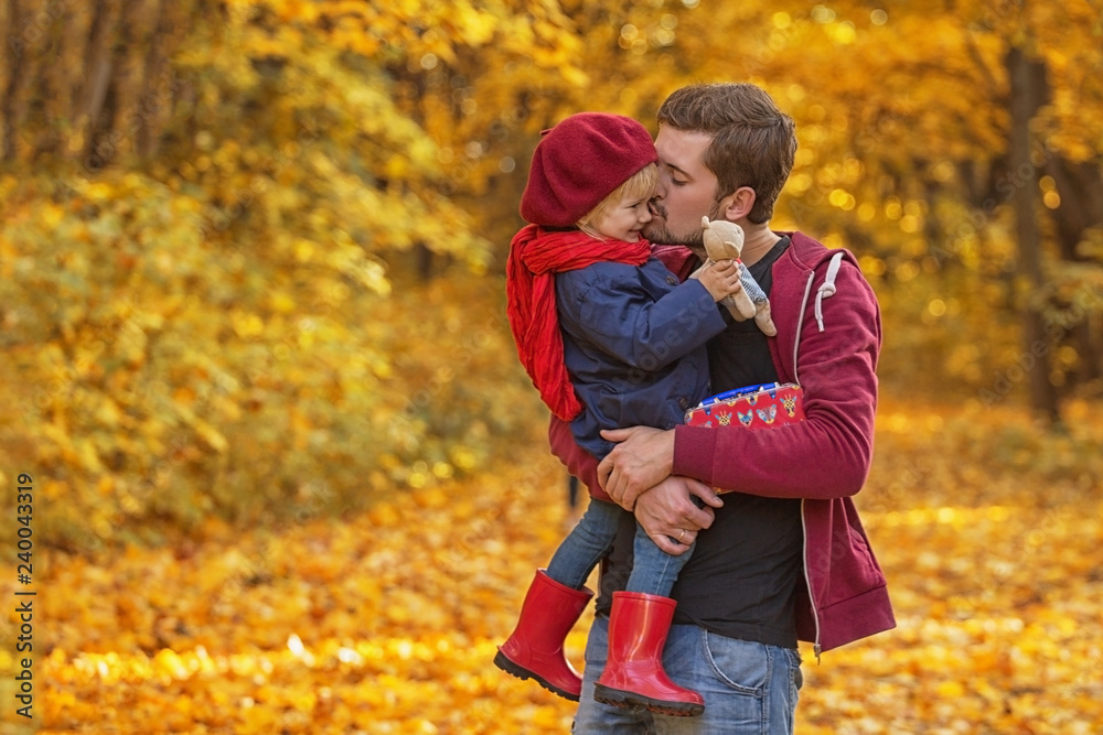 Father hugs and kisses his daughter in autumn day. The girl is holding a teddy bear. Father hugs and kisses his daughter in autumn day. The girl is holding a teddy bear.