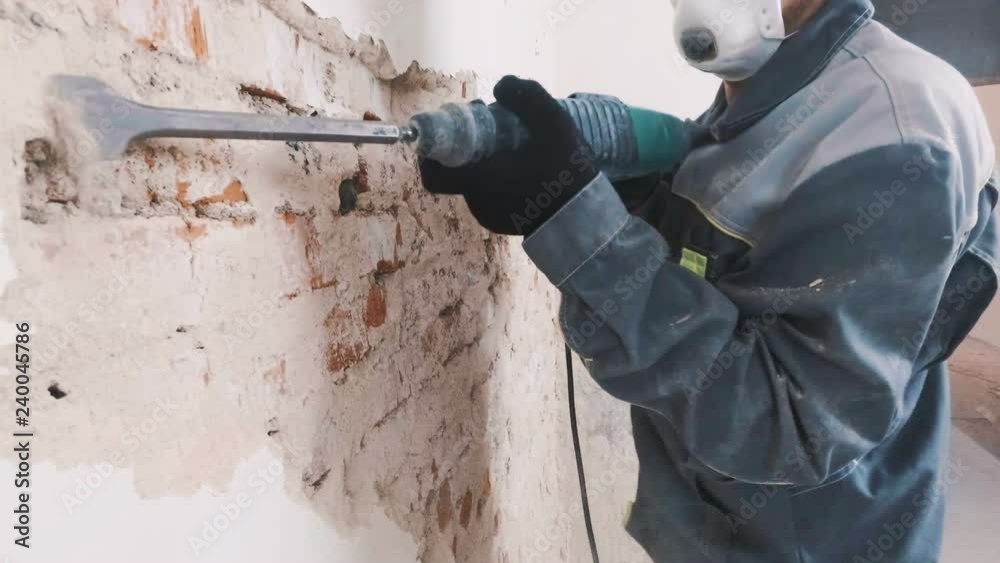 worker in protective suit demolishes plaster wall. Dirty, hard work. Personal protective equipment. Helmet, respirator and goggles.
