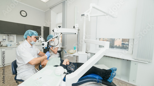 Doctor used microscope. Dentist is treating patient in modern dental office. Operation is carried out using cofferdam. Client is inserted and restored teeth  make denture.