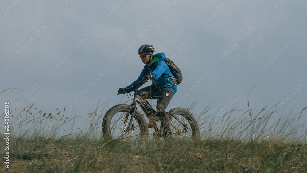 Fat bike also called fatbike or fat-tire bike in summer driving through the hills. The guy is riding a bike along the sand and grass high in the mountains. He performs some tricks and runs dangerously