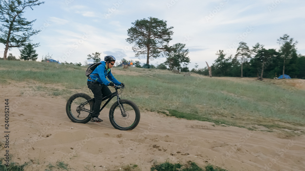 Fat bike also called fatbike or fat-tire bike in summer driving through the hills. The guy is riding a bike along the sand and grass high in the mountains. He performs some tricks and runs dangerously Fat bike also called fatbike or fat-tire bike in summer driving through the hills. The guy is riding a bike along the sand and grass high in the mountains. He performs some tricks and runs dangerously