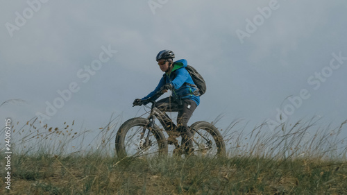 Fat bike also called fatbike or fat-tire bike in summer driving through the hills. The guy is riding a bike along the sand and grass high in the mountains. He performs some tricks and runs dangerously