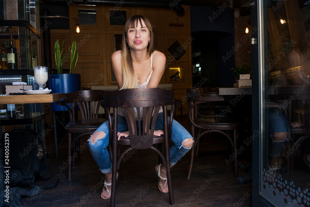 young pretty cute girl sitting in a cafe on a chair in jeans emotional pleasing and sexy