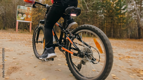 One caucasian children rides bike road in autumn park. Little girl riding black orange cycle in forest. Kid goes do bicycle sports. Biker motion ride with backpack and helmet. Mountain bike hardtail.