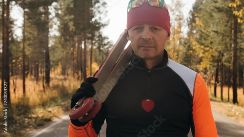 Training an athlete on the roller skaters. Biathlon ride on the roller skis with ski poles, in the helmet. Autumn workout. Roller sport. Adult man riding on skates.The athlete goes and holds sports photo