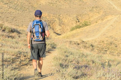 Man tourist walks on the steppe with a backpack on his back and a cap