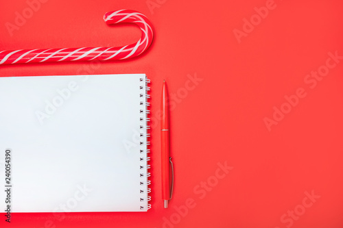 Christmas flatlay with clean spring pad, red pen and candy canes on the bright red background.