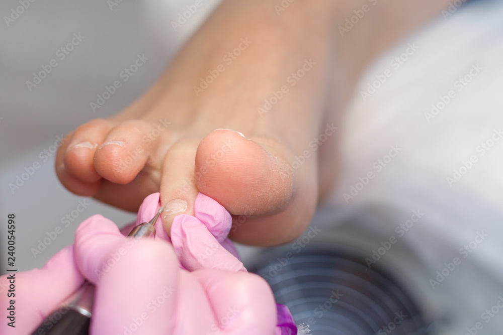 Naklejka premium Professional hardware pedicure using pink gloves and electric device machine. Patient on medical pedicure procedure, visiting podiatrist. Peeling feet. Foot treatment in SPA salon.Podiatry clinic.