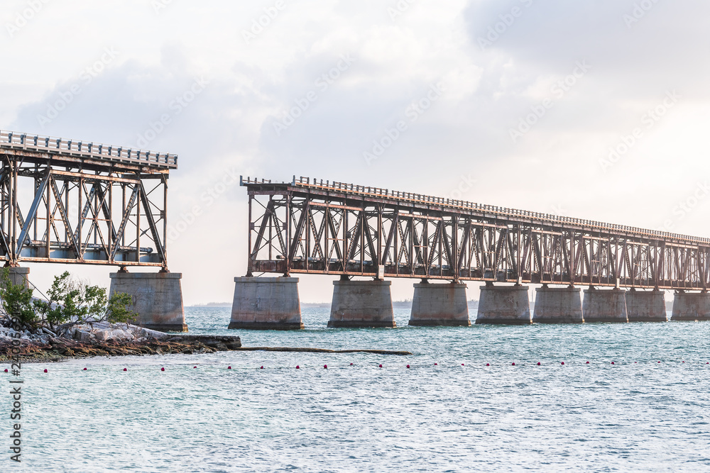 Old, rusted, rust, rusty derelict Bahia Honda rail road bridge in state park with view on shore, coast, tree, clouds, cloudy blue sky at sunset, dusk, horizon, ocean, sea water