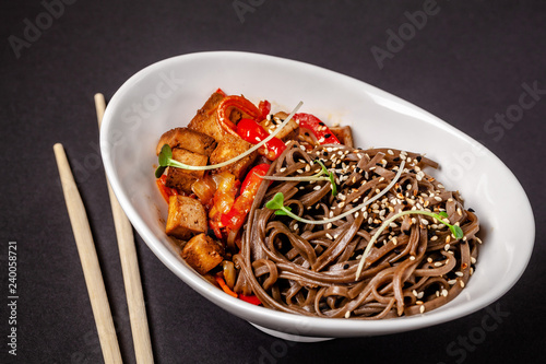 Concept of Asian cuisine. Buckwheat noodles with vegetables and tofu. Carrots, bell peppers, white and black sesame. Japanese or Chinese dish.