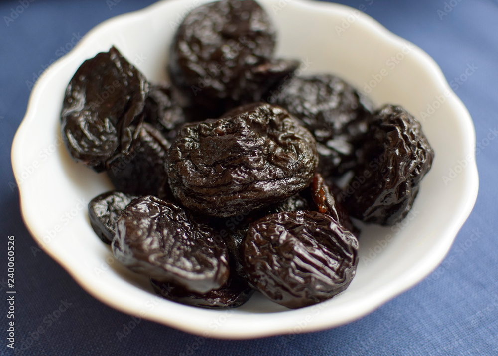 Dried plum in a white bowl on a blue background Dried plum in a white bowl on a blue background