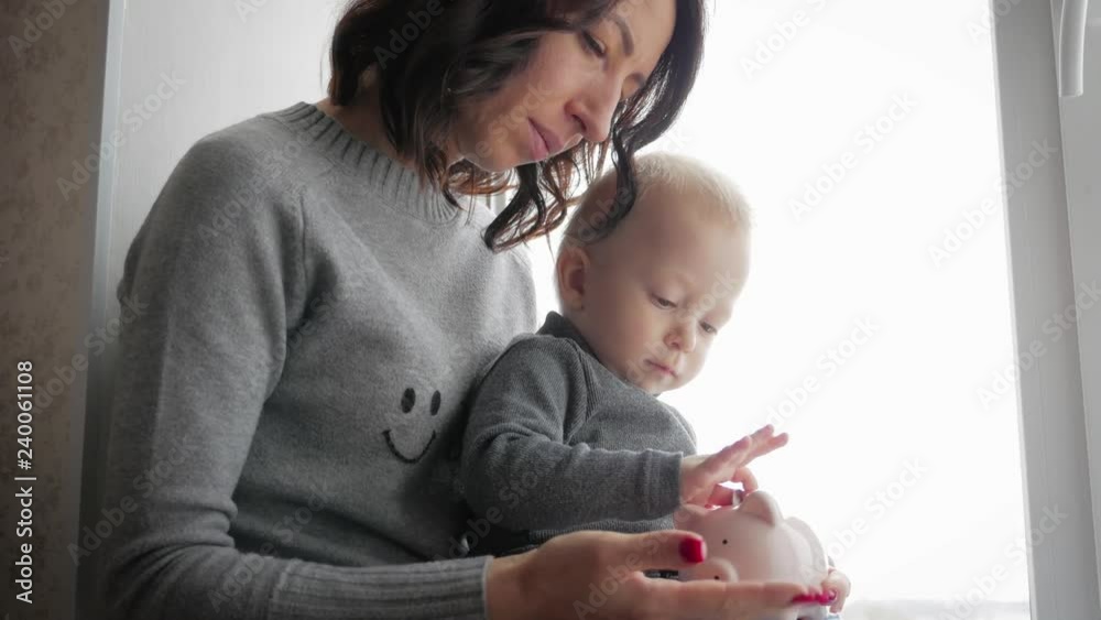 Mother and little son putting coins into piggy bank for the future savings.