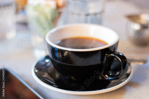 Black and White Cup and Saucer Of Black Coffee On Breakfast Table Next To Cellular Phone