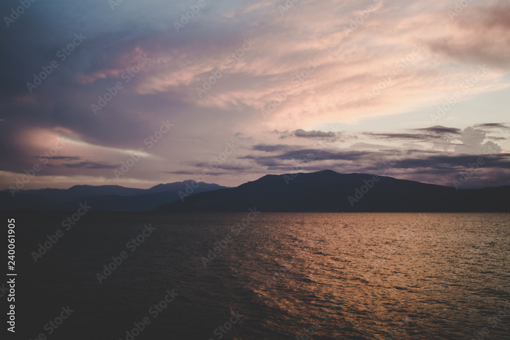 abstract evening twilight time after sunset outdoor landscape view with dark mountain ridge silhouettes shape near sea calm water surface wallpaper pattern unfocused concept