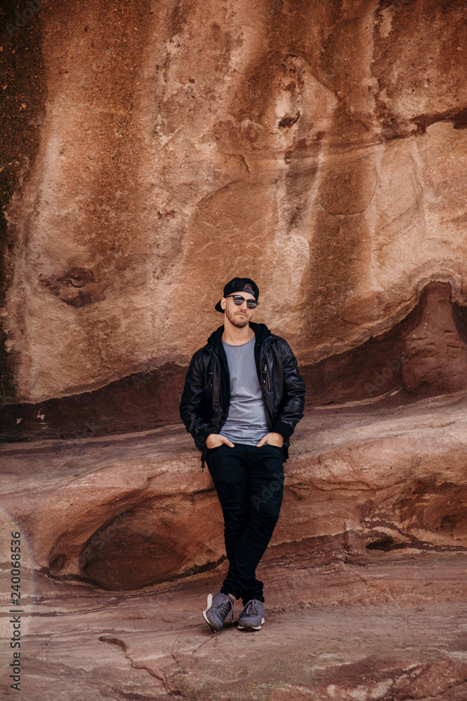 Portrait of Young Good Looking Casual Traveling Handsome Man Smiling Near Ancient Desert Red Rocks in Jacket Outside Portrait of Young Good Looking Casual Traveling Handsome Man Smiling Near Ancient Desert Red Rocks in Jacket Outside