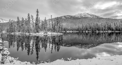 Light snow covered trees and mountain with reflection on lake