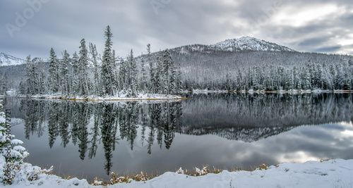 Light snow covered trees and mountain with reflection on lake