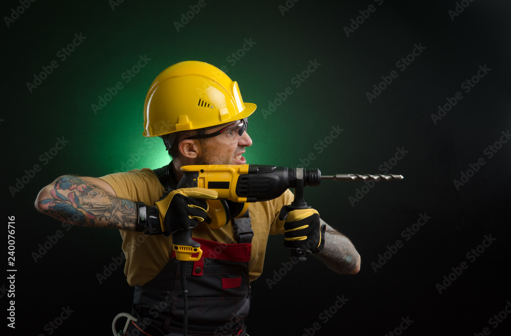 a young man posing on a black background in a work uniform and a construction tool
