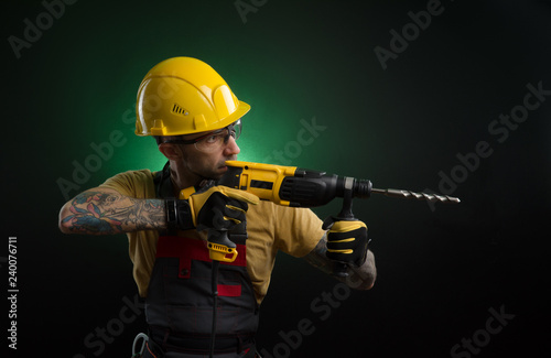 a young man posing on a black background in a work uniform and a construction tool