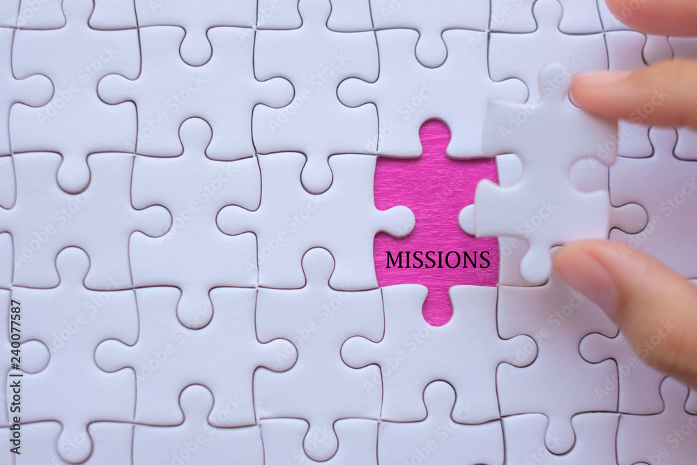 Woman Hand holding white jigsaw puzzle piece with words MISSIONS. Business resolutions, success, goals and strategy concept Woman Hand holding white jigsaw puzzle piece with words MISSIONS. Business resolutions, success, goals and strategy concept