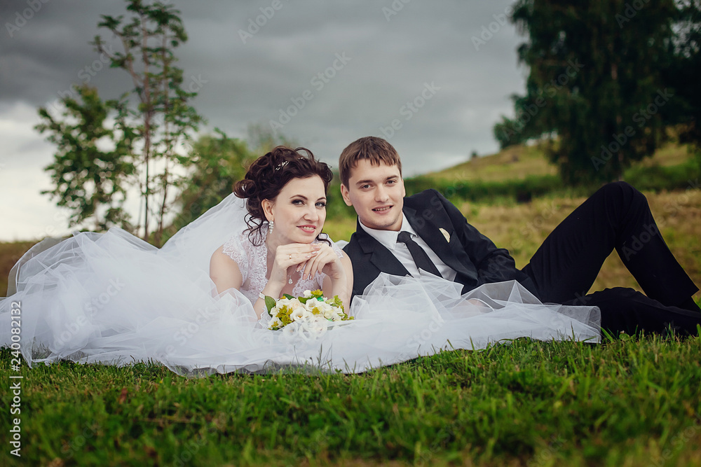 Happy bride and groom sit summer on the grass in the Park and enjoy each other