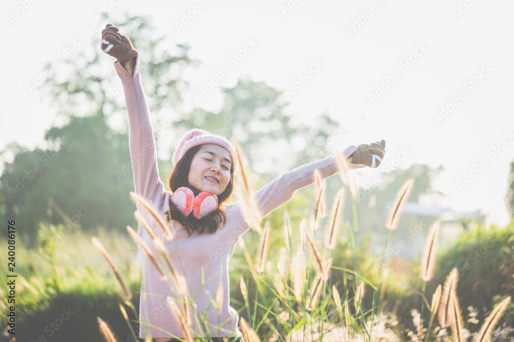 Young woman standing outdoor with warm clothes and gloves and earmuff with a holding hands up on a warm morning background. Young woman standing outdoor with warm clothes and gloves and earmuff with a holding hands up on a warm morning background.