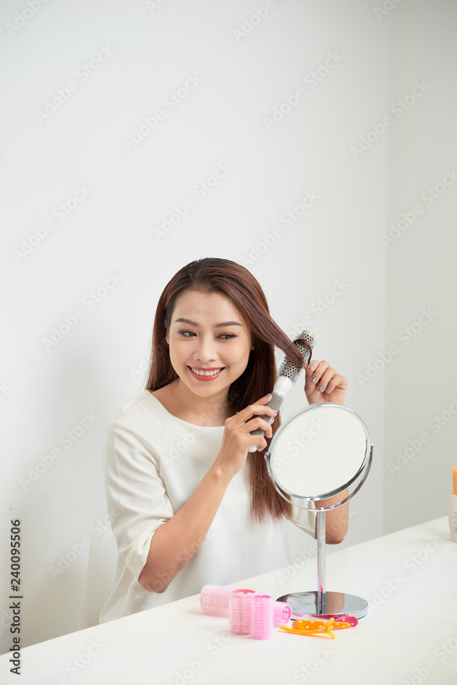 Getting rid of tangles. Beautiful young woman looking at her reflection in mirrorand brushing her long hair while sitting at the dressing table Getting rid of tangles. Beautiful young woman looking at her reflection in mirrorand brushing her long hair while sitting at the dressing table