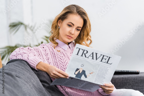 attractive woman sitting on sofa and reading travel newspaper in living room