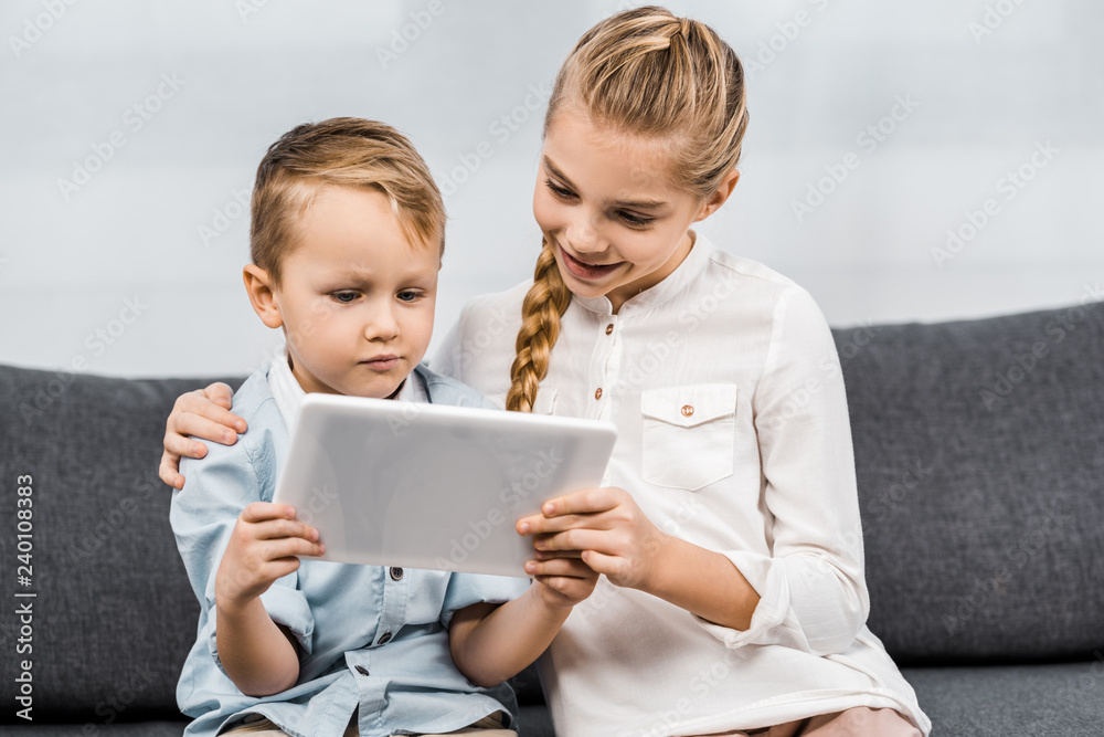 cute siblings sitting on sofa and using digital tablet in living room cute siblings sitting on sofa and using digital tablet in living room