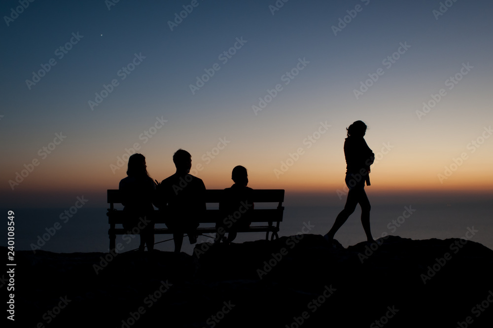 silhouette of a person on a sunset. Three people sitting on a bench and one woman is leaving