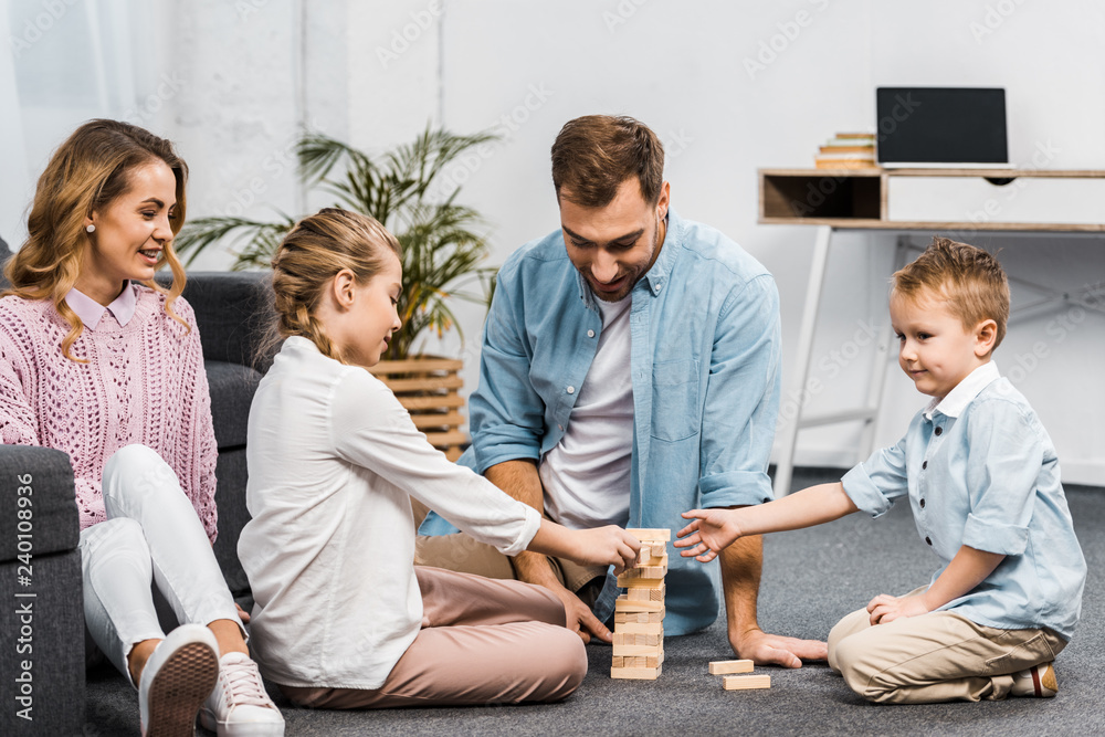 two parents playing blocks wood tower game with daughter and son on floor in living room two parents playing blocks wood tower game with daughter and son on floor in living room