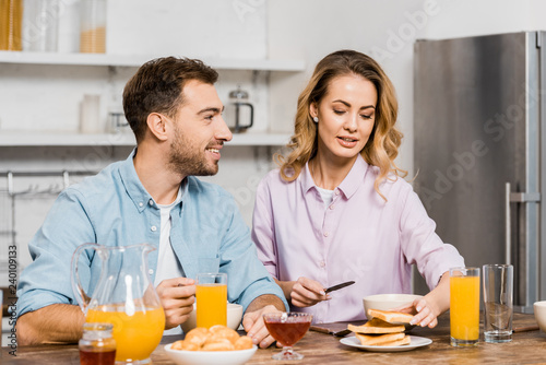 handsome man looking at pretty woman holding knife and toast in kitchen