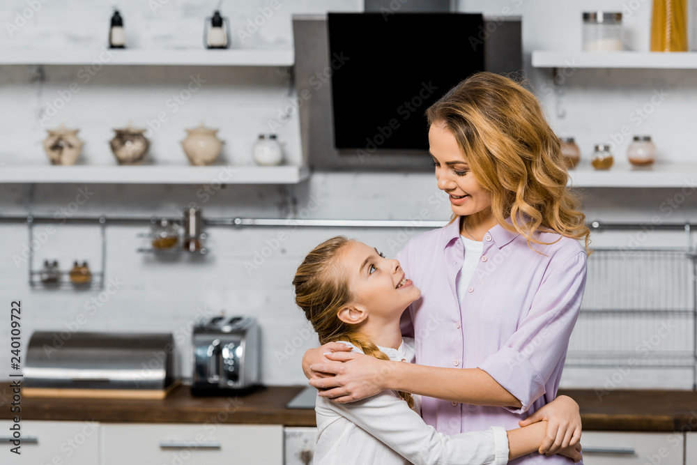 pretty woman and cute daughter hugging and looking at each other in kitchen pretty woman and cute daughter hugging and looking at each other in kitchen