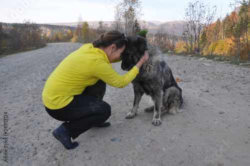 A woman and a Caucasian Shepherd dog are sitting nearby on the road.