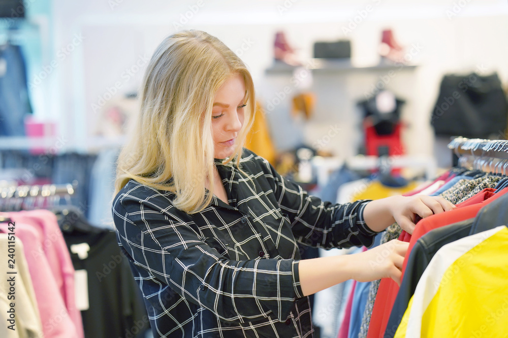 Young blonde girl, choose new things in the store. Beautiful young female shopper chooses liked things in the boutique. A young girl chooses things on a hanger in a store. Second hand shop. Young blonde girl, choose new things in the store. Beautiful young female shopper chooses liked things in the boutique. A young girl chooses things on a hanger in a store. Second hand shop.