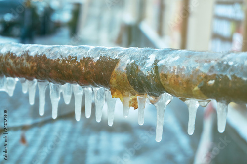 Many small icicles have frozen on a rusty pipe in the street in the winter