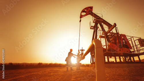 Oil worker is checking the pump near oil derrick on the sunset background.