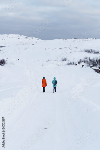 during the expedition, two girls in warm bright jackets go on a snow-covered white hill on a frosty day somewhere in the north beyond the Arctic Circle © Александр Коновалов