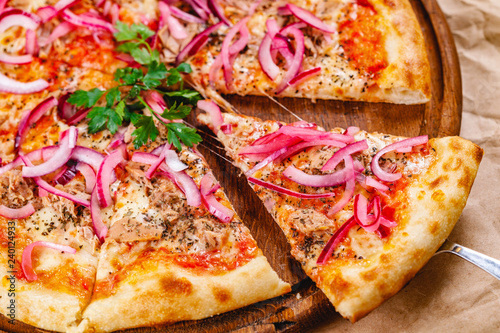 Pizza with tuna and red onion on wooden cutting board. Close up
