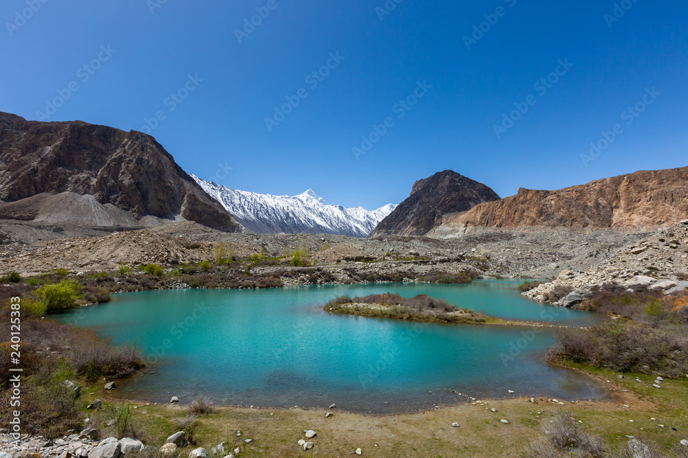 Panorama shot of small turquoise mountain lake under the sunny day with blue sky along Karakorum Highway in Passu, Hunza district of Pakistan.