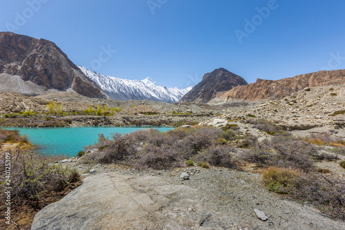 Panorama shot of small turquoise mountain lake under the sunny day with blue sky along Karakorum Highway in Passu, Hunza district of Pakistan.