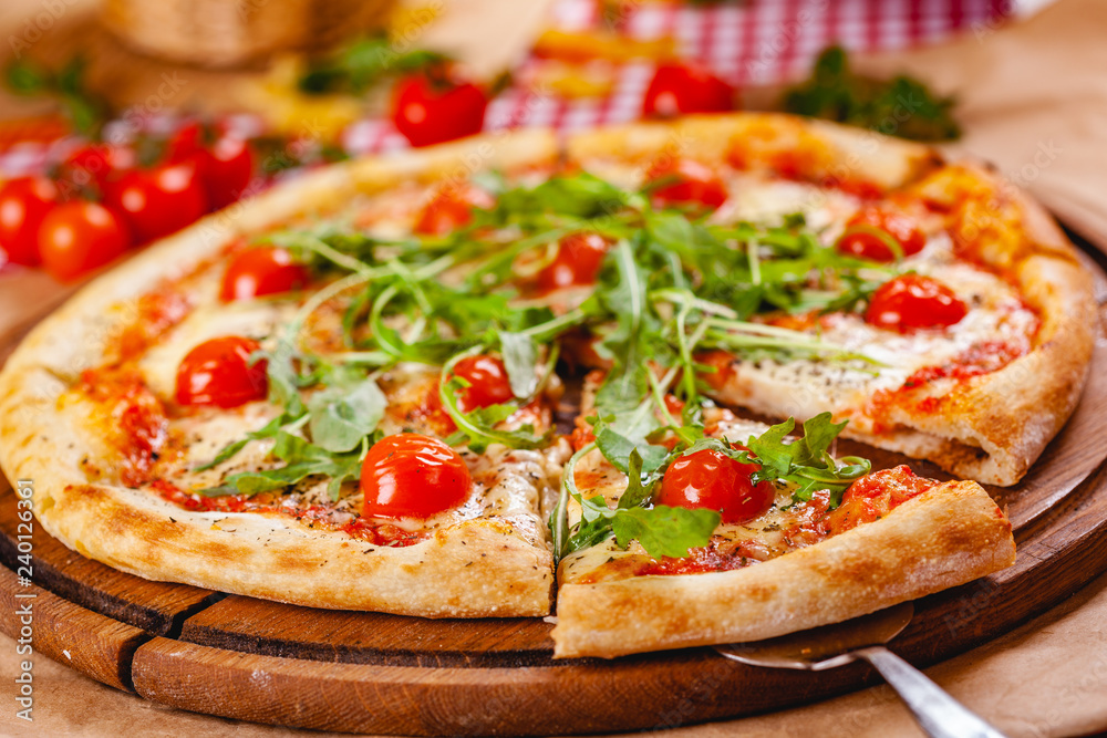Italian Pizza with tomatoes, mozzarella cheese and arugula on wooden cutting board. Close up Italian Pizza with tomatoes, mozzarella cheese and arugula on wooden cutting board. Close up