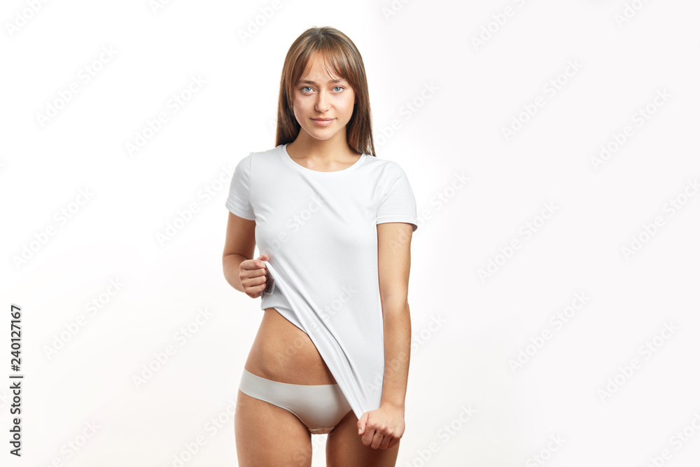 Young attractive woman with soft and smooth healthy skin after laser depilation of her private parts. Slim woman seductively raising up her white t-shirt, isolated on white background. Young attractive woman with soft and smooth healthy skin after laser depilation of her private parts. Slim woman seductively raising up her white t-shirt, isolated on white background.