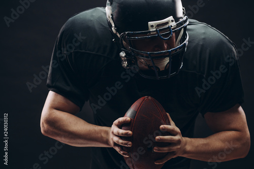 American football player with black helmet and armour running in motion, holding ball, getting ready to score a goal, close up shot over dark background photo