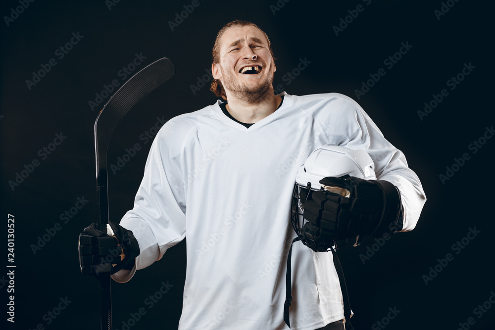 Obraz premium Portrait of cheerful proud caucasian hockey player smiling with teeth, looking in camera with happy and relaxed face expression, posing after victory in hockey match with stick, isolated on white