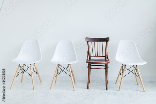 Modern style of three plastic chairs versus Vintage style of one brown wooden chair with background of white painted wall for loft decoration idea of house  office or shop