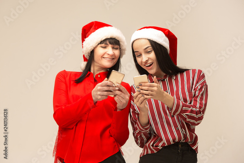 Happy family in Christmas sweater posing with mobile phones. Enjoying love hugs  holidays people. Mom and doughter on a gray background in the studio